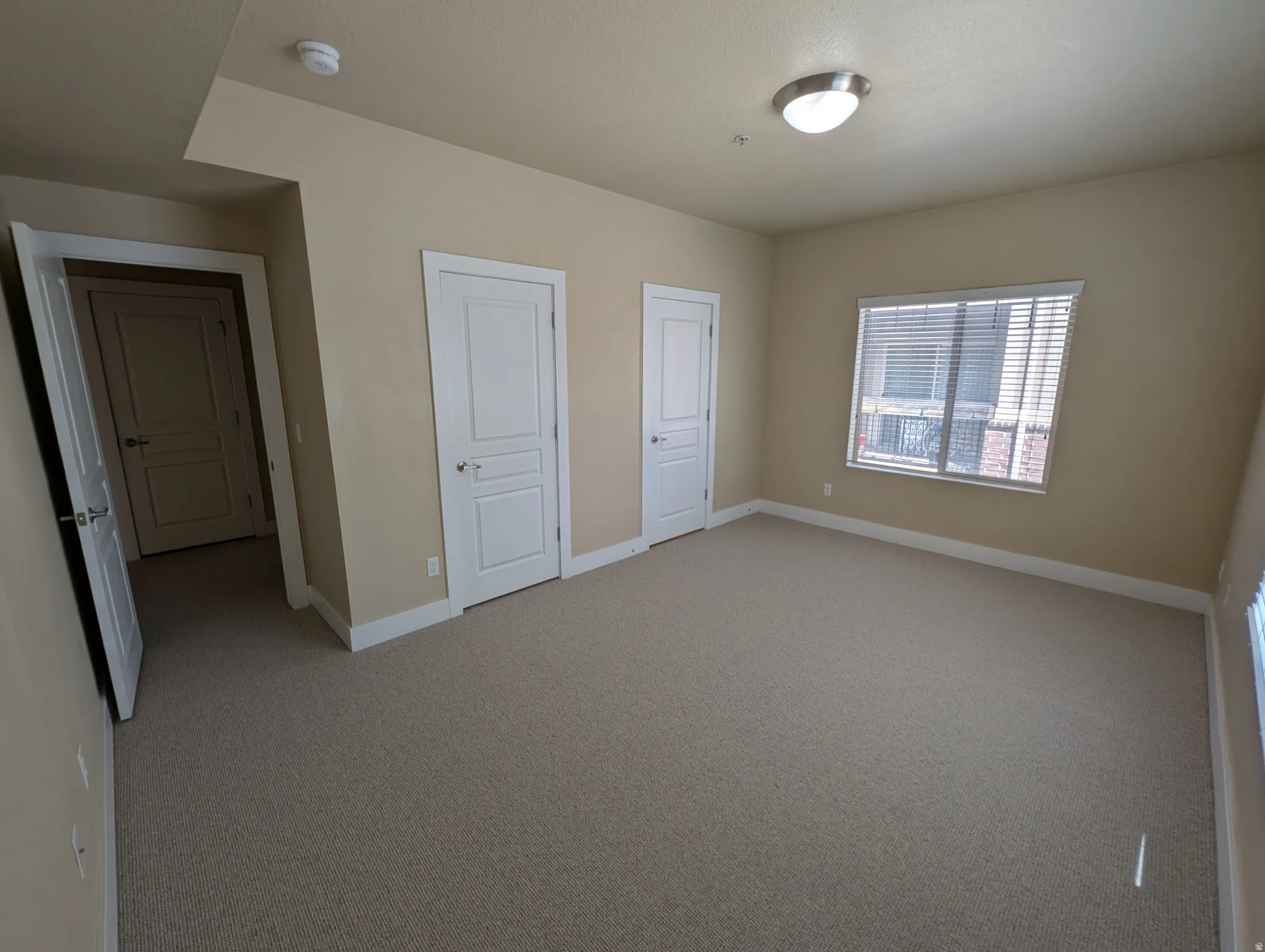 Spacious room with neutral-toned carpeting, light beige walls, and white baseboards