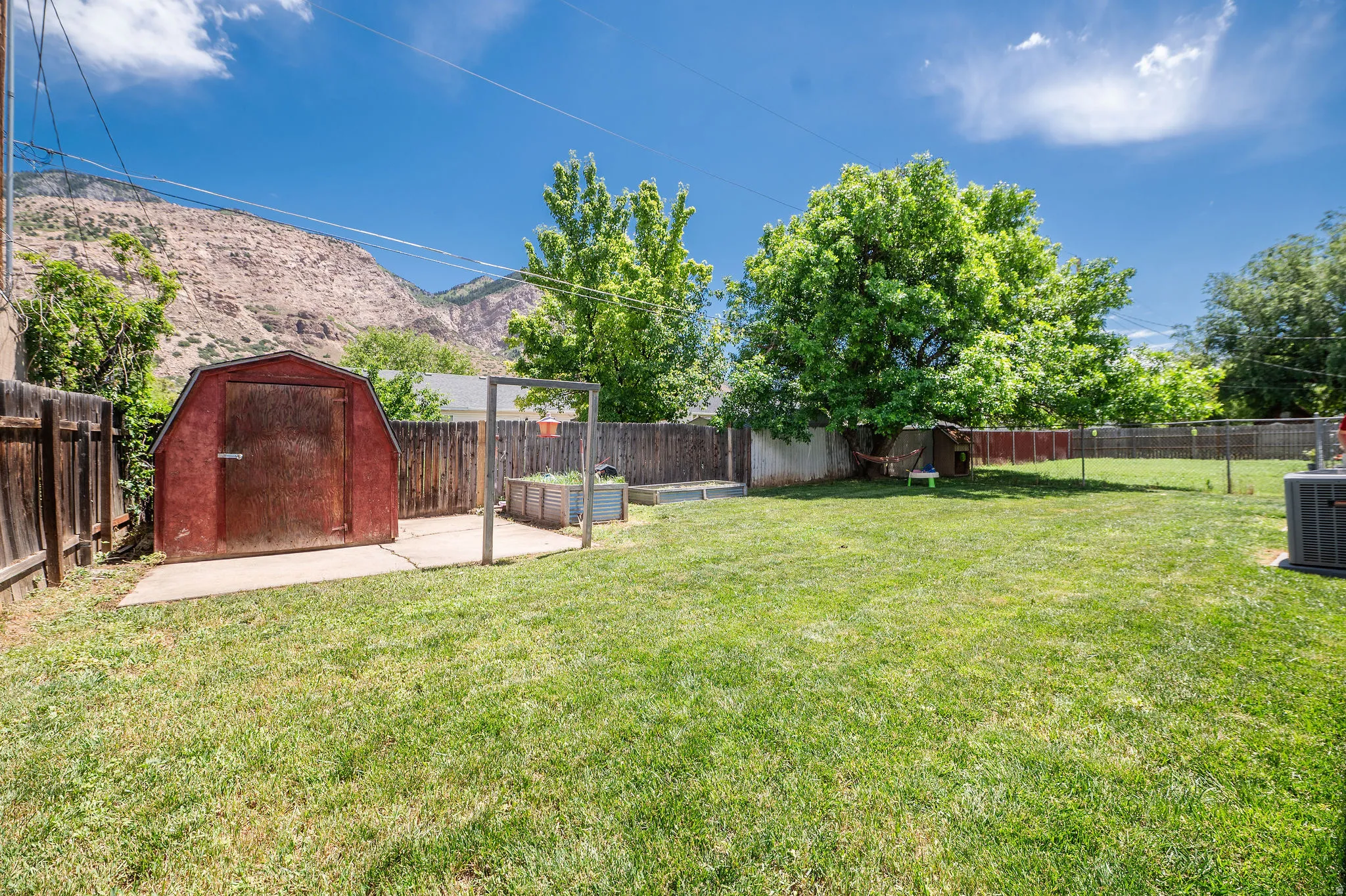 Spacious backyard with mountain views featuring a manicured lawn, mature trees, shed on a concrete pad, and a wooden privacy fence.