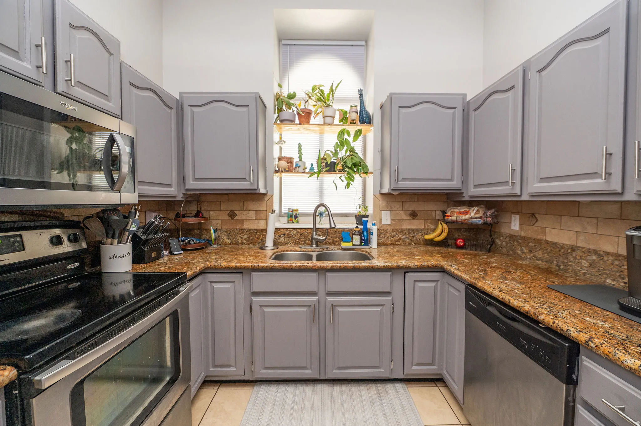 Kitchen featuring painted light gray cabinets, granite countertops, stainless steel appliances, and tile backsplash.