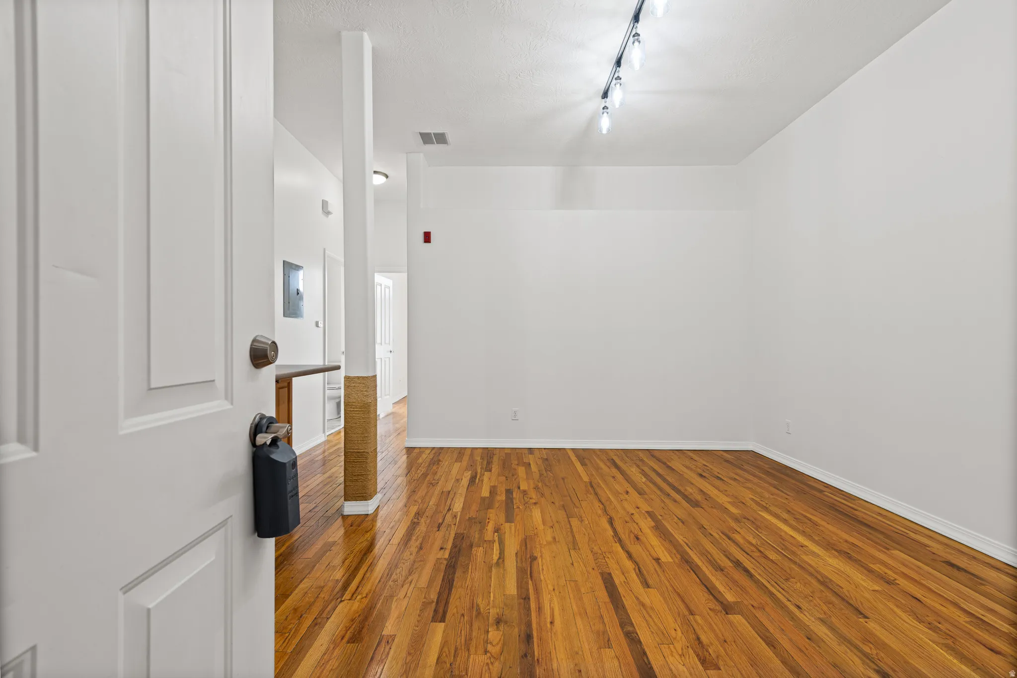 Spacious room featuring rich wood-finish flooring, crisp white walls, and contemporary track lighting