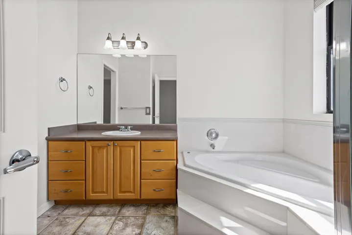 Bathroom featuring a corner soaking tub, a single vanity with wood cabinetry, and a walk in shower to the left.