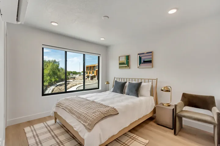 Bright bedroom featuring a large window with black framing, recessed lighting, wood-finish flooring, and a wall-mounted mini-split HVAC unit