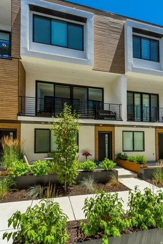 Modern facade featuring multi-level balconies with black railings, horizontal wood siding accents, and large windows