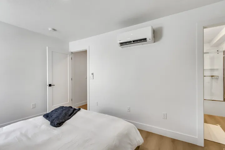 Interior room featuring white walls, wood-finish flooring, a wall-mounted climate control unit, and a flat-panel door with matte black hardware