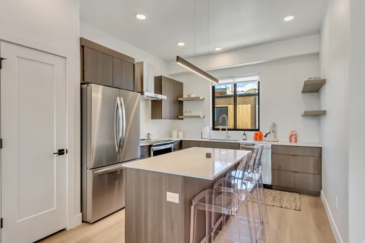 Modern kitchen featuring a central island with a light-toned countertop, stainless steel appliances, wood-finish cabinetry, light wood-finish flooring, and recessed lighting