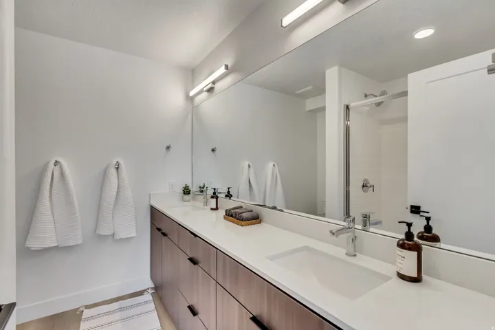 Bathroom vanity with integrated sink, white countertop, wood-finish cabinetry, and matte black hardware