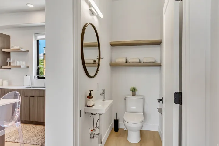 Compact powder room featuring a wall-mounted sink, oval mirror, and light wood-finish flooring