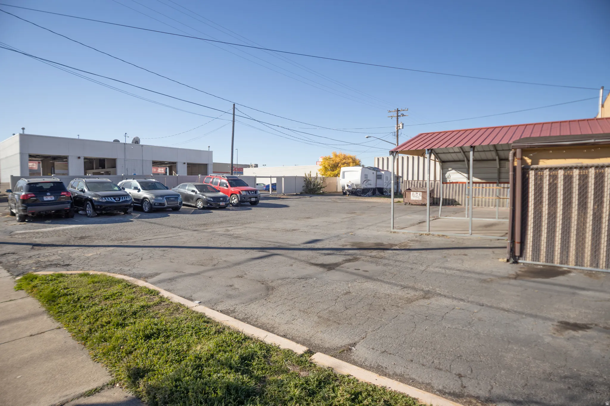 Paved parking lot with a corrugated metal fence and a covered structure featuring a red metal roof