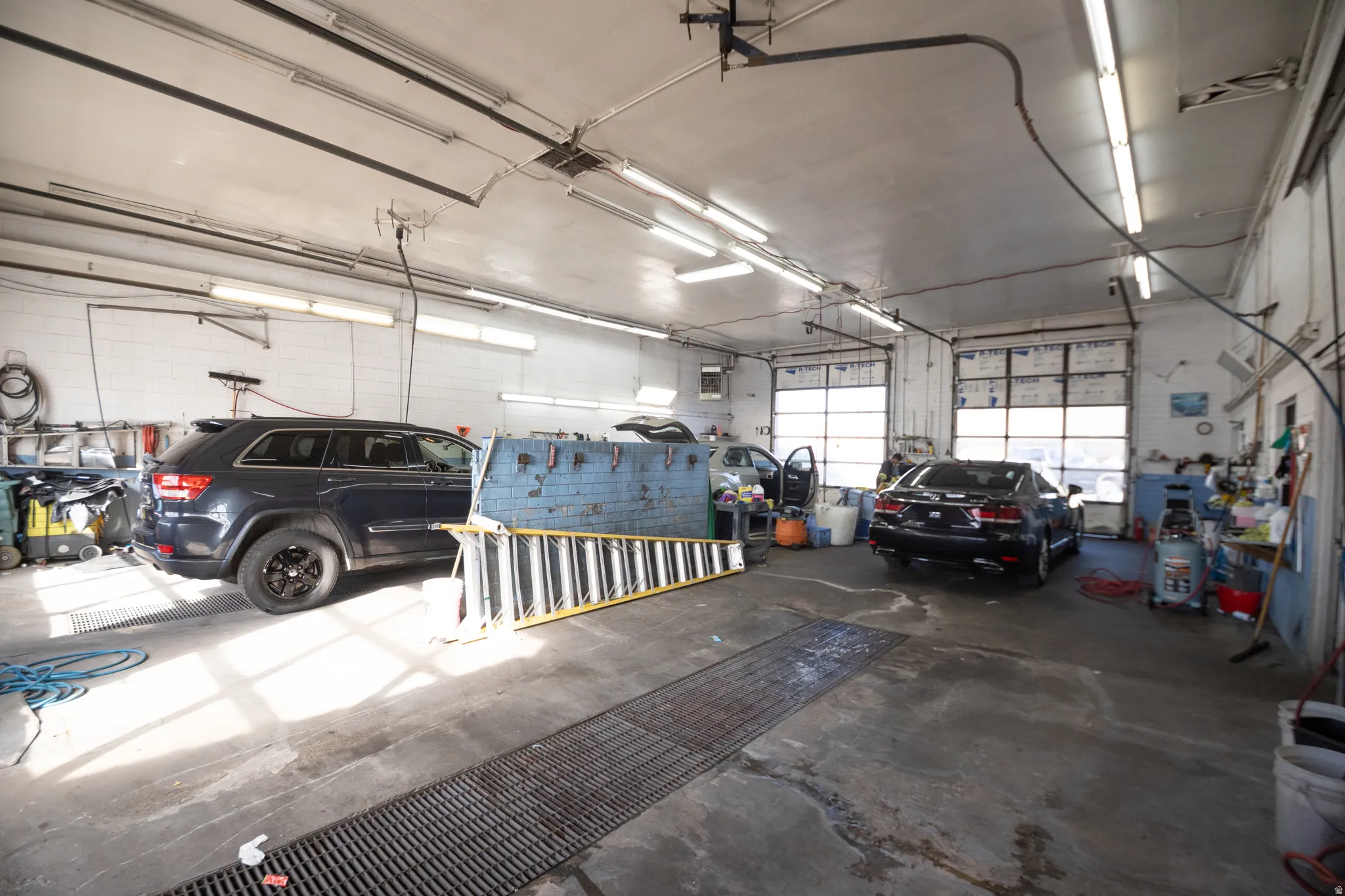 Industrial-style garage featuring multiple roll-up doors, high ceilings, concrete flooring with integrated grates, and overhead fluorescent lighting