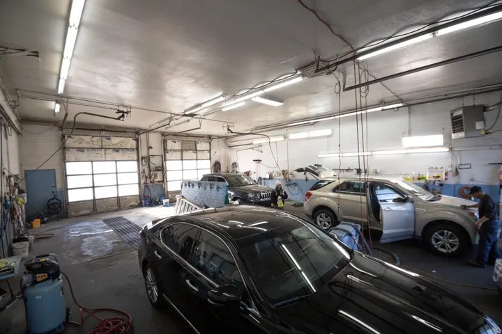 Spacious commercial garage featuring two overhead bay doors, concrete flooring, exposed overhead lighting, a wall-mounted heating unit, and a side access door