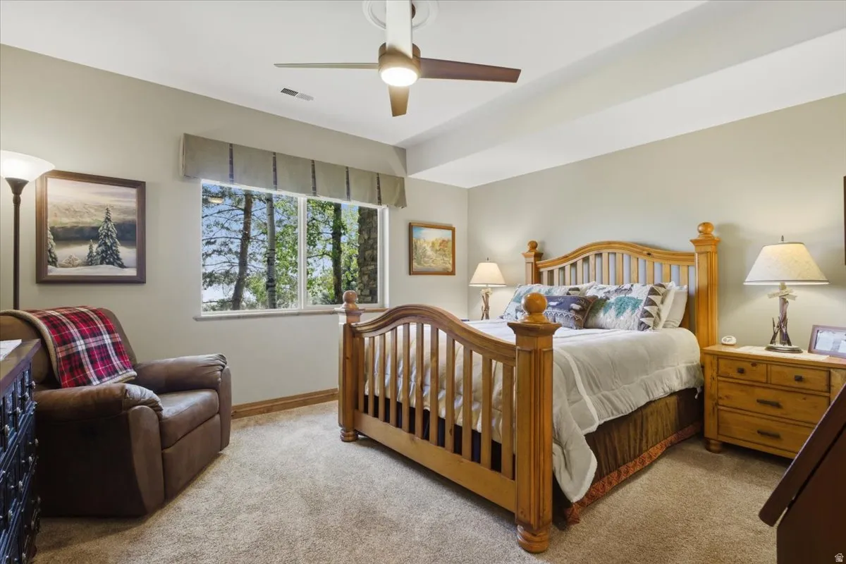 Bedroom featuring a ceiling fan, a window with exterior tree scenery, light-colored carpeting, and light beige wall paint