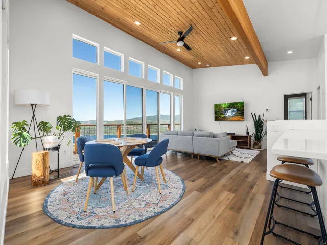 Expansive living area featuring soaring vaulted ceilings with wood paneling and exposed beams, large format windows, wood-finish flooring, and a built-in kitchen island with a white countertop