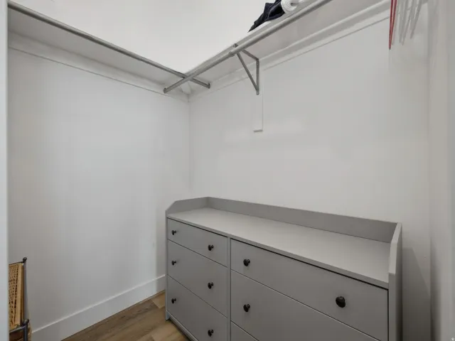 Walk-in closet featuring light wood-finish flooring, white walls, and built-in metal clothing rods