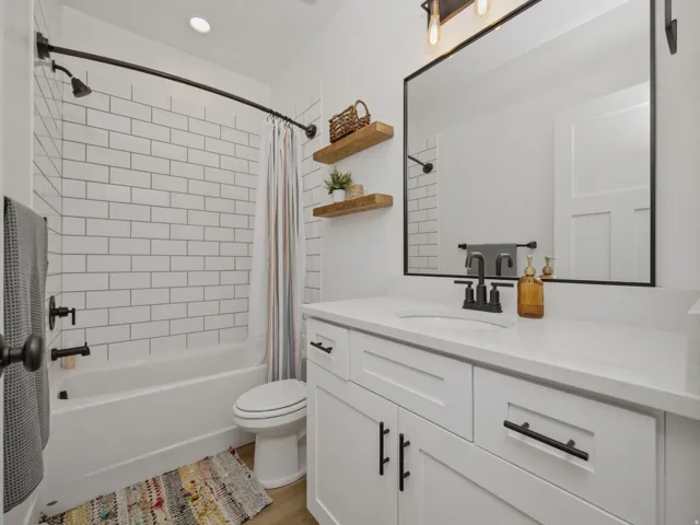 Bathroom featuring a white subway tile shower surround, dark bronze fixtures, a white vanity with a light-toned countertop, a rectangular mirror, and wood-finish flooring
