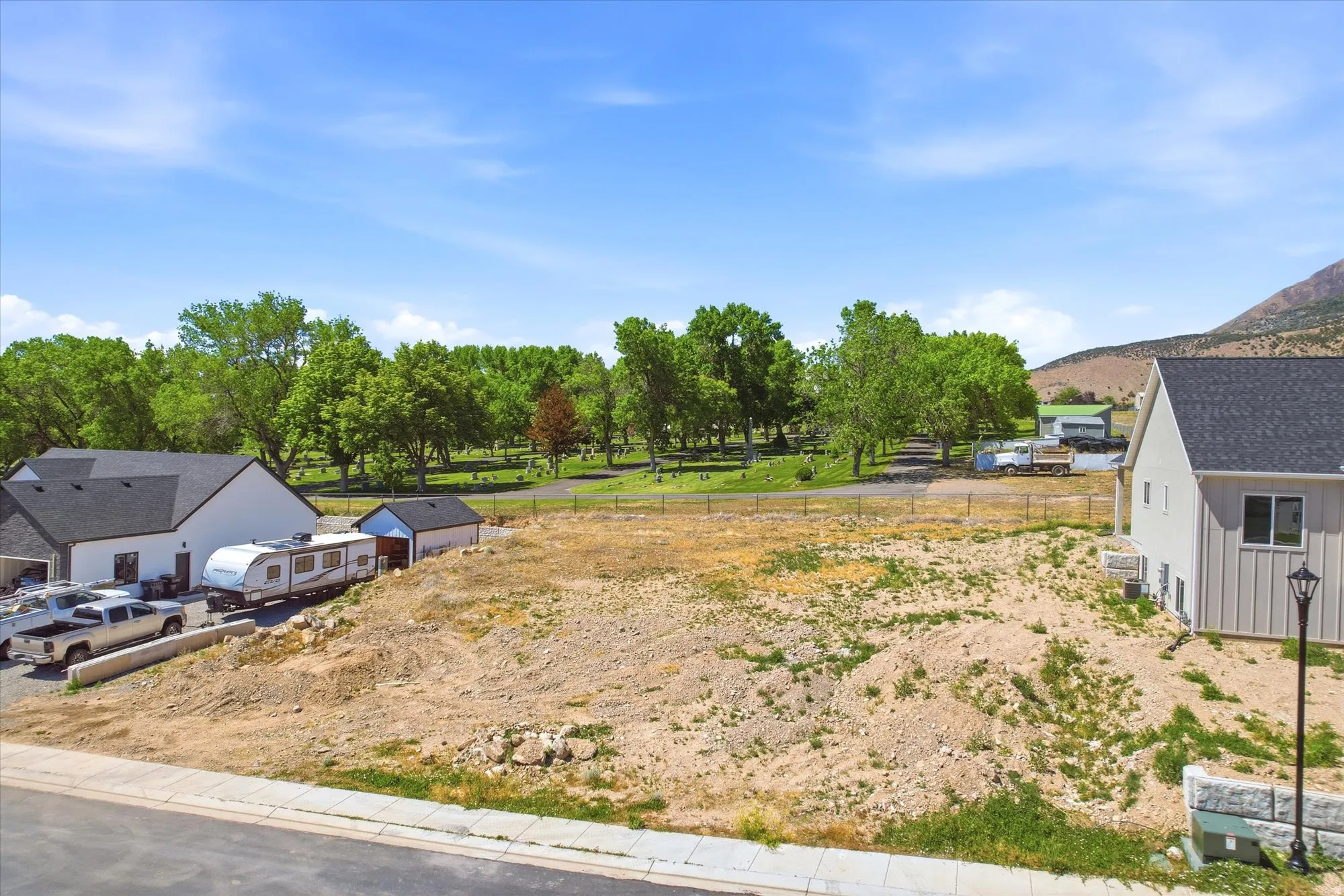 Expansive undeveloped lot presenting building potential, with a paved road frontage, partially established stone retaining wall, and proximity to mature trees