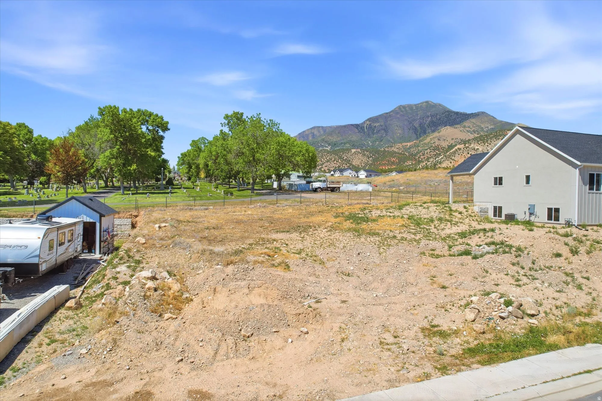 Large undeveloped lot featuring a mountainside backdrop and a single-story outbuilding with a dark roof