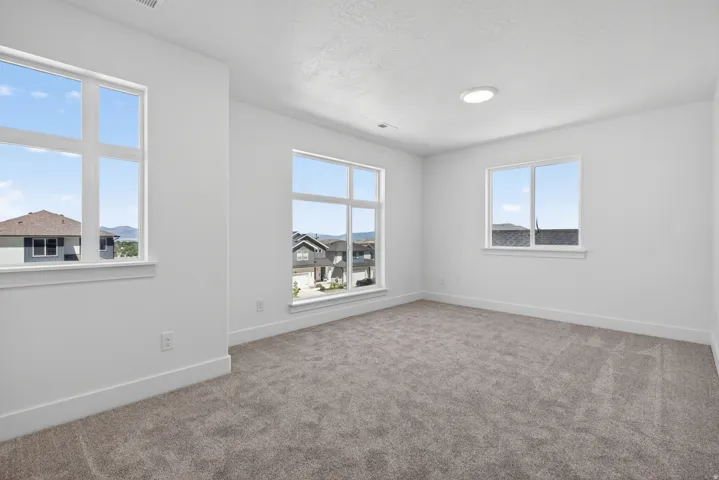 Bright interior space featuring a neutral color palette, grey textured carpeting, white baseboards, and multiple large windows with white trim