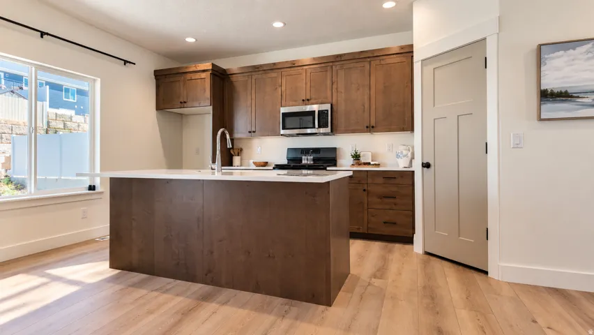 Kitchen featuring a large island with white countertop, wood-finish flooring, stainless steel appliances, and recessed lighting