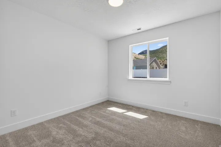 Neutral interior room featuring a large window, textured carpeting, crisp white walls, and a baseboard trim