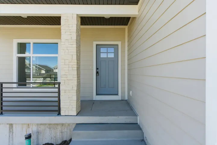 Inviting front entrance featuring a light gray door, white trim windows, stacked stone column, horizontal metal railing, and light beige siding