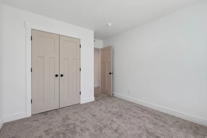 Neutral-toned room featuring a closet with bi-fold doors, white trim, light gray textured carpeting, and a white ceiling