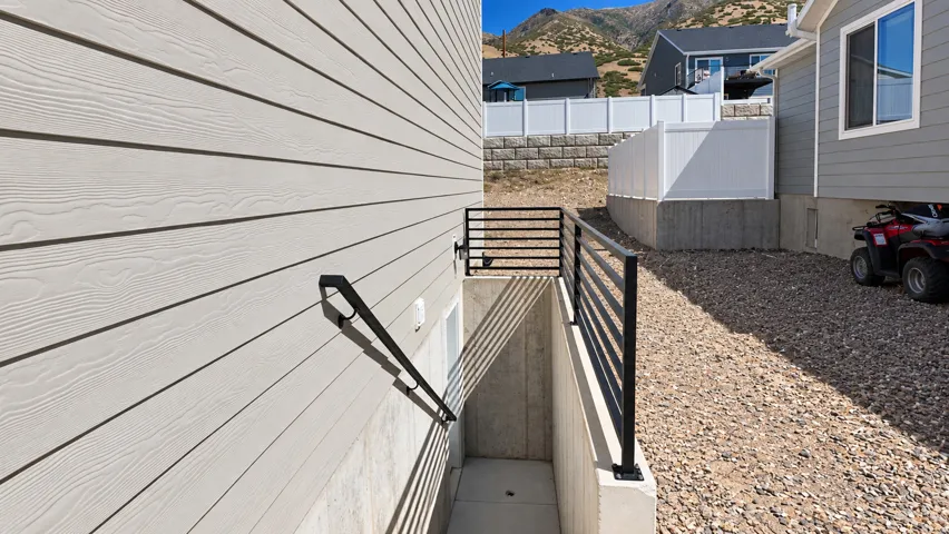 Siding exterior, black metal railing, concrete retaining wall, gravel ground cover, white privacy fence