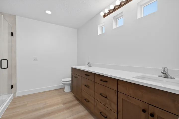 Double vanity with white countertop and integrated sinks, wood-finish cabinetry, and matte black hardware