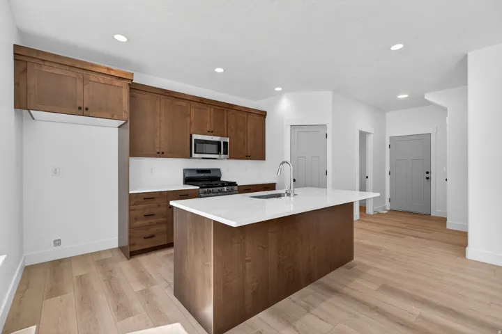 Kitchen featuring a central island with an undermount sink, wood-finish cabinetry, stainless steel appliances, and light-toned countertops