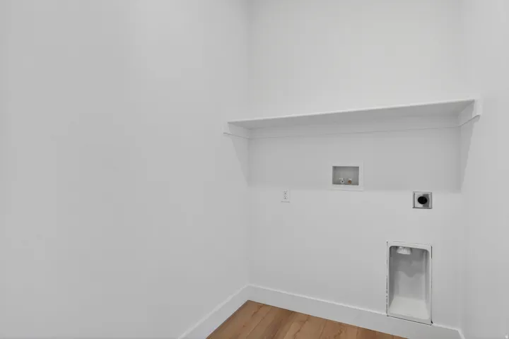 Laundry area featuring wood-finish flooring, white walls, and a built-in shelf