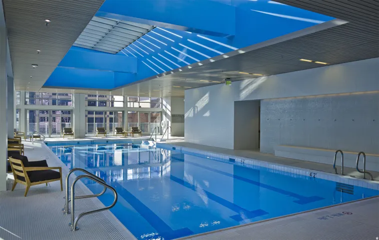Indoor lap pool featuring a skylight, full-height window walls, and perimeter seating