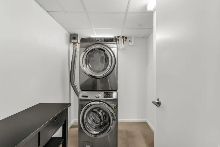 Dedicated laundry area featuring stacked front-loading appliances, a drop ceiling, and light-toned flooring