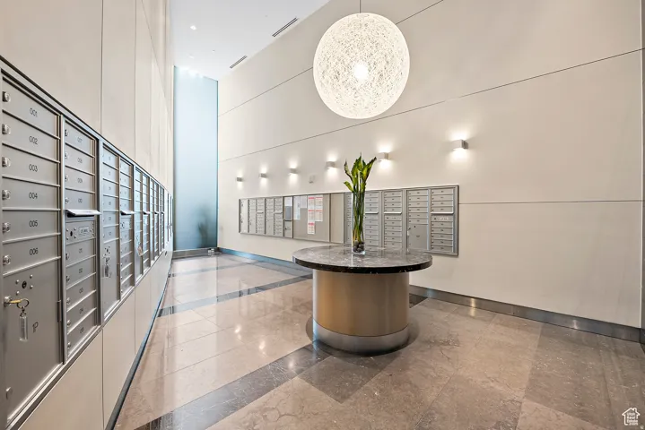 Building lobby featuring extensive mailboxes, a large orb pendant light, wall sconces, a circular table with a stone top, and polished tile flooring with contrasting accents