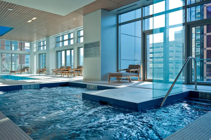 Indoor hot tub with blue tile surround, glass partition, and stainless steel grab rail