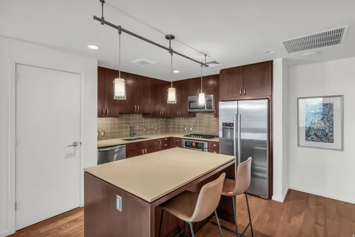 Kitchen featuring a center island with countertop seating, rich wood-finish cabinetry, stainless steel appliances, tile backsplash, and wood-finish flooring