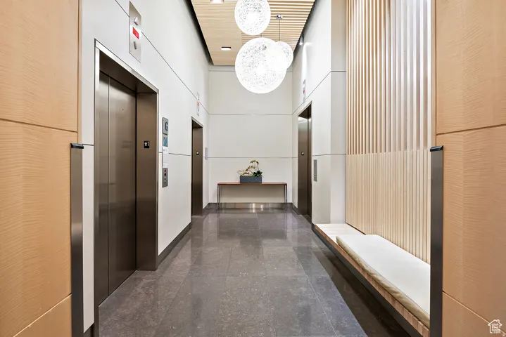 Modern lobby featuring two stainless steel elevators, dark stone tile flooring, and wood-paneled walls
