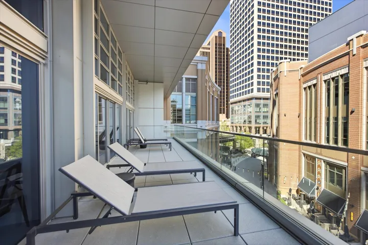 Spacious private balcony featuring a glass railing, smooth concrete flooring, and multiple sets of floor-to-ceiling windows