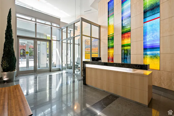 Lobby featuring a contemporary reception desk with a black stone countertop and under-counter lighting, vibrant floor-to-ceiling art panels, light wood wall paneling, and polished stone flooring