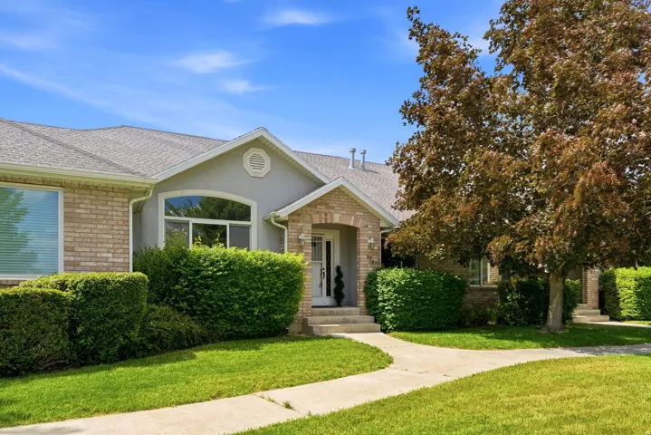 Front exterior featuring a brick and stucco facade, an arched entryway, established landscaping, a concrete pathway, and a mature tree