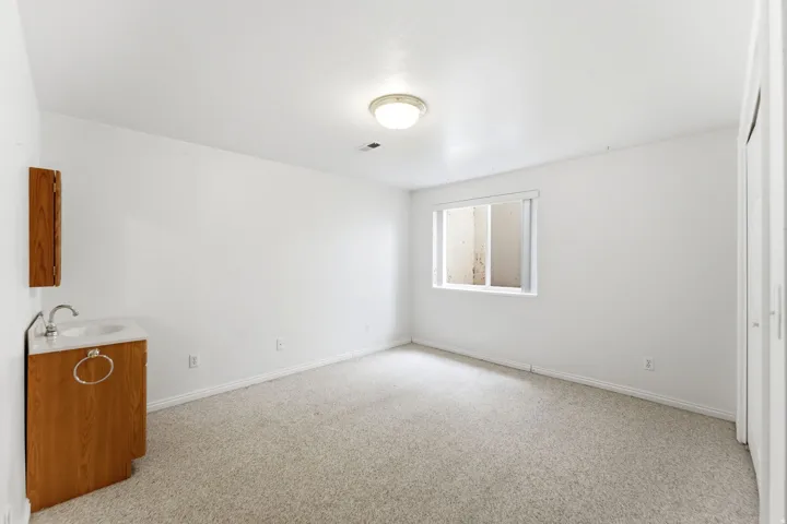 Carpeted room featuring a white single-hung window with a window well, a ceiling-mounted light fixture, and a built-in wood-finish vanity with an integrated sink and wall-mounted medicine cabinet