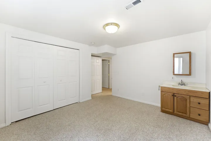 Carpeted room featuring a double bi-fold closet, light wood-finish vanity with a sink, framed wall mirror, and flush-mount ceiling light fixture