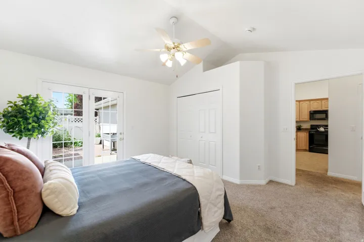 Vaulted ceiling bedroom with ceiling fan, dual bi-fold closet doors, and French patio doors opening to an outdoor paver patio