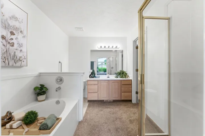 Bathroom featuring a built-in soaking tub, a dual vanity with a light wood-finish cabinet, and a framed glass shower enclosure