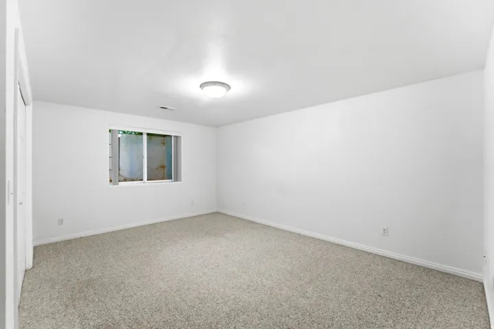 Spacious room featuring neutral carpeting, white painted walls, and a single window