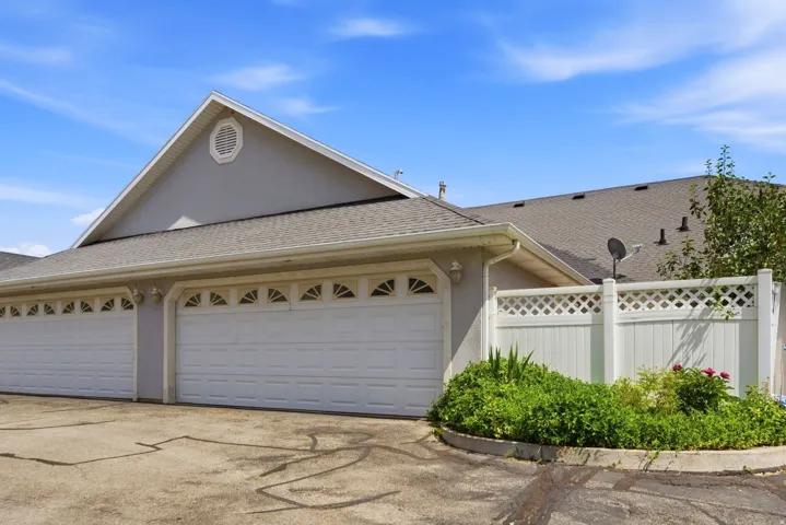 Two white garage doors with arched window inserts, a light gray stucco exterior, and a peaked roofline featuring an octagonal vent