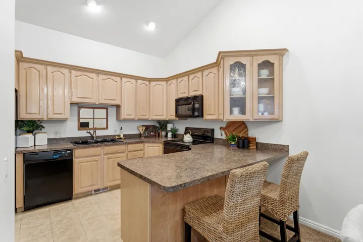 Kitchen featuring a peninsula breakfast bar, light wood-finish cabinetry, black appliances, and durable countertop surfaces