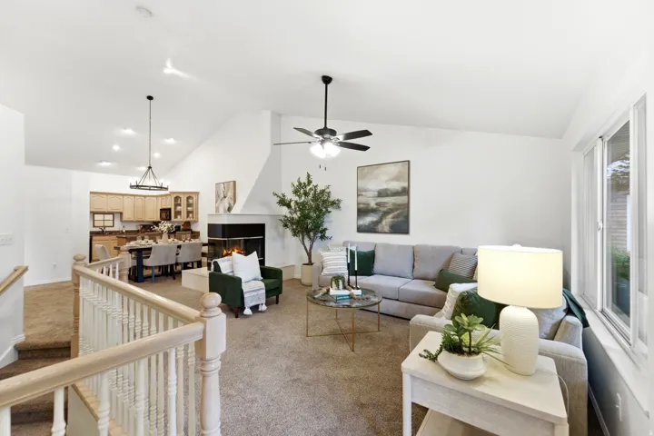 Vaulted ceilings and abundant natural light highlight this open concept living space featuring a fireplace, ceiling fan, and carpeted flooring