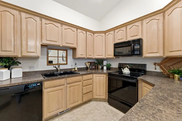 Kitchen featuring light wood cabinetry with arched details, dark laminate countertops, and a black double-basin sink