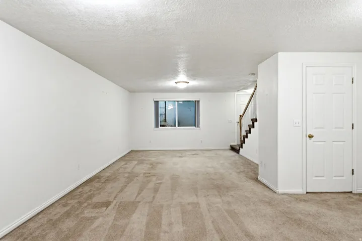 Spacious room featuring neutral carpeting, white painted walls, and a window providing natural light
