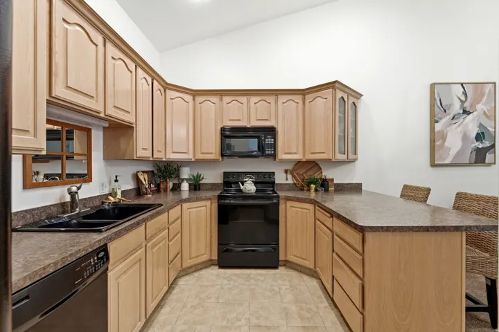 U-shaped kitchen featuring light wood cabinetry, dark countertops, a black double-basin sink, and black appliances including a range and microwave