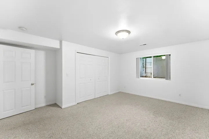 Carpeted room with white walls, featuring a window and two sets of bi-fold closet doors